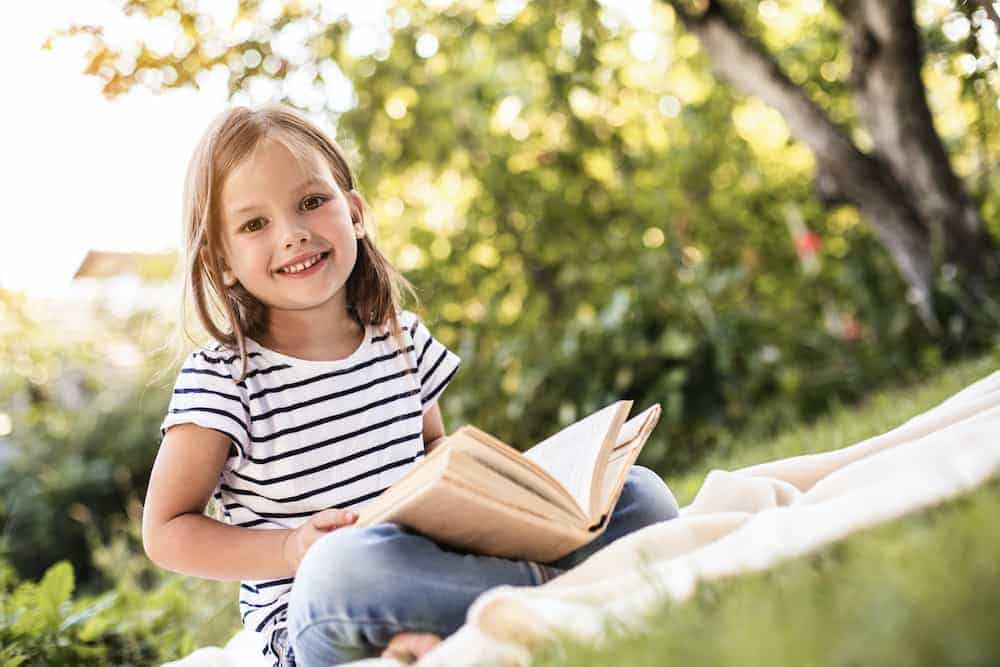 Lebenszahl 4 Kinder: Mädchen mit Buch auf Wiese